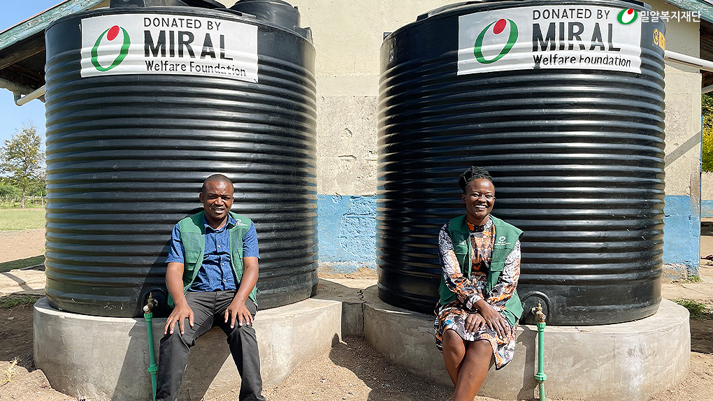설치된 물탱크 앞에 앉아 있는 밀알복지재단 케냐 직원들.jpg